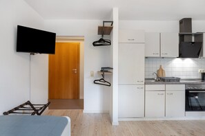 Eine kleine Küche mit weißen Schränken, einem eingebauten Backofen und einer Holztür im Hintergrund.