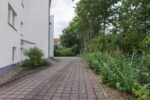 Ein gepflasterter Weg führt zu einem Gebäude mit weißer Fassade und einem Fenster.