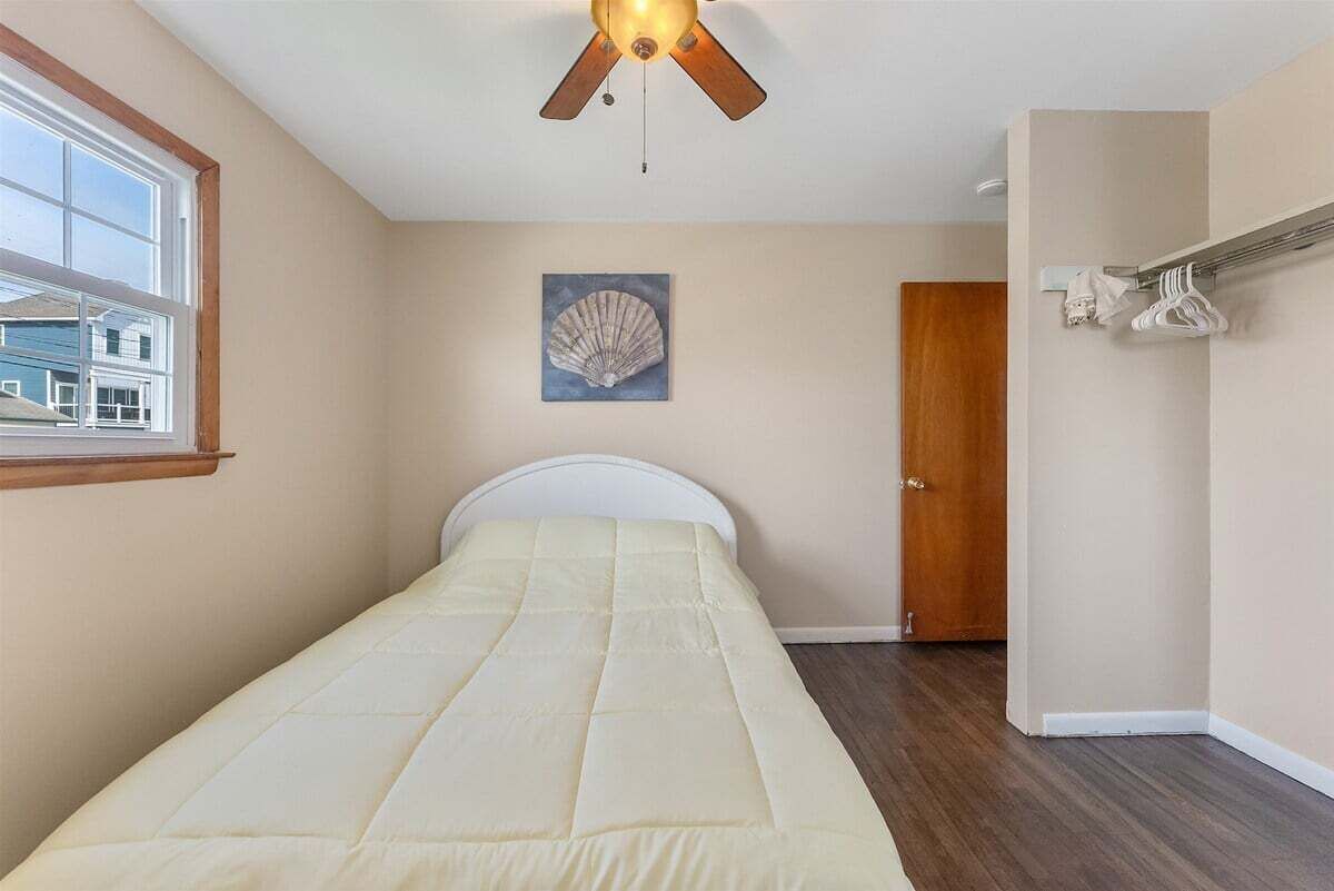 Un dormitorio con cama, ventilador de techo, un cuadro, una puerta y una ventana.