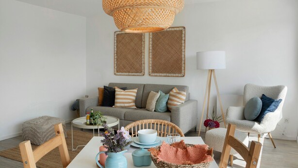 A living room with a sofa, chairs, a table with decorative items, a rattan light fixture, and a floor lamp.