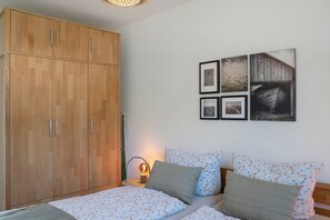 Une chambre avec une armoire en bois, un lit avec une literie à motifs floraux et un mur orné de tableaux encadrés.