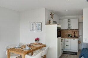 A compact kitchen with white cabinetry, a wooden dining table, and a small seating area.