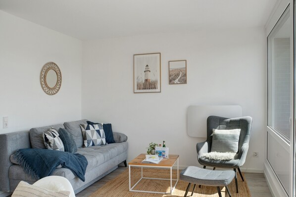 A modern living room with a grey sofa, a coffee table, a grey armchair, and a large window.