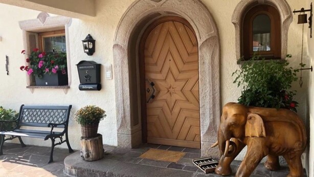 A wooden door with a star pattern, a bench, a potted plant, and a stone wall. - Apartment '2' with Mountain View, Shared Garden and Wi-Fi (Krün)