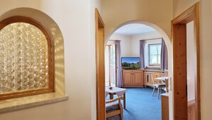 A hallway leading to a dining area with a table and chairs, a television, and a window with curtains. - Apartment '2' with Mountain View, Shared Garden and Wi-Fi (Krün)