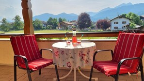 Un balcón con dos sillas a rayas rojas, una mesa con mantel floreado y una jarrón de vidrio grande con bebidas.