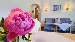 A room with a floral sofa, a small table, and a vase with a pink and white flower. - Apartment '2' with Mountain View, Shared Garden and Wi-Fi (Krün)