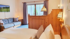 Ein Hotelzimmer mit Bett, Sofa, Holz-Kopfseitenverkleidung, einem Fenster mit Vorhängen, einer Lampe und einem Wand-Fernseher.