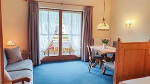 Ein Zimmer mit einer Couch, einem Esstisch mit Stühlen, einer Chandelier und Blick durch eine Glastür.