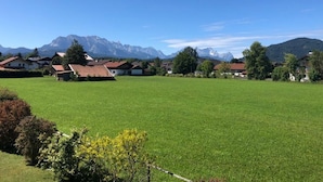 Ein beschauliches Dorf mit Häusern, einem großen grünen Feld und Bergen im Hintergrund.