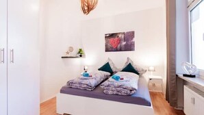A bedroom with a bed, bedside tables, a wall-mounted shelf with decorative items, and a window with curtains. - Central & bright | 4 persons (Magdeburg)