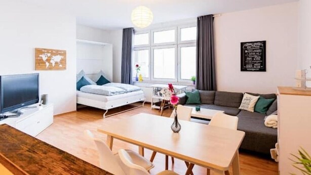 A modern living room with a sofa, a dining table, a TV, and a bed. - Central & bright | 4 persons (Magdeburg)