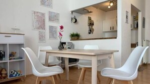 A dining area with a white table and chairs, a wooden floor, and a kitchen in the background. - Central & bright | 4 persons (Magdeburg)