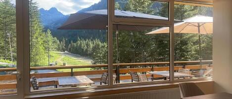 A room with large windows overlooking a mountainous landscape, wooden furniture, and a view of a deck area.