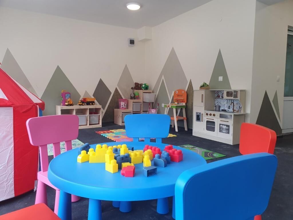 Un área de juegos para niños con una mesa azul, sillas de colores y varios juguetes.