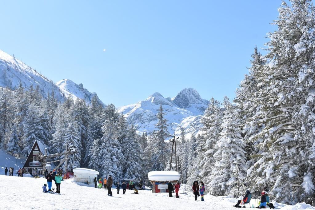 A snowy mountain scene with a ski lift, a lodge, and snow-covered trees.