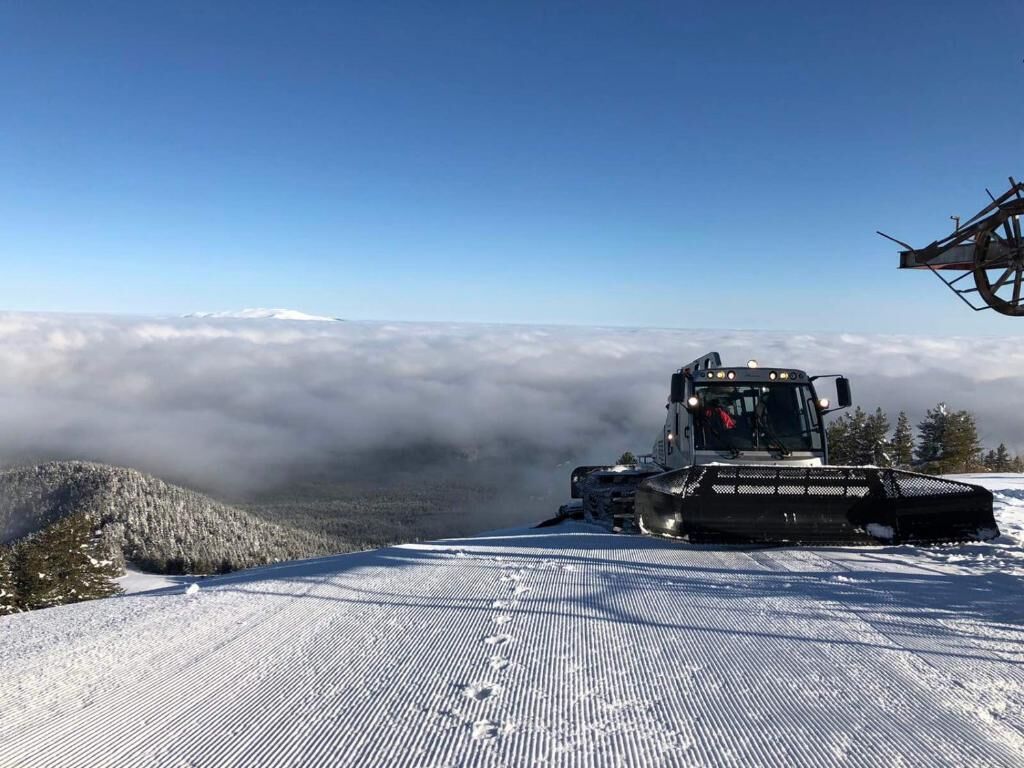 A snow-covered landscape with a large vehicle on a ski slope.