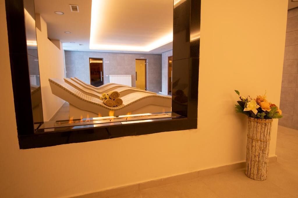 Uma área de recepção com design moderno, apresentando um balcão de atendimento, um espelho refletindo o interior e um vaso com flores.