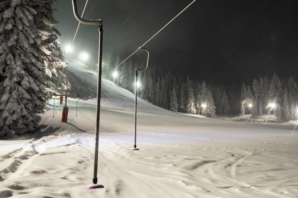 Pista de esquí nevada de noche con cables y luces de telesilla.