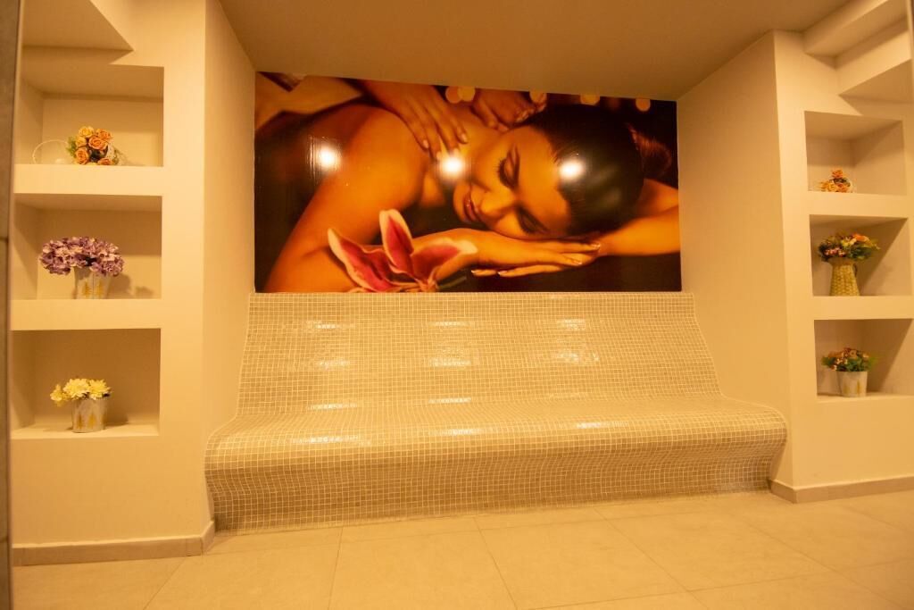 Uma área de spa com um banco revestido de azulejos, prateleiras com flores e um grande painel decorativo na parede.