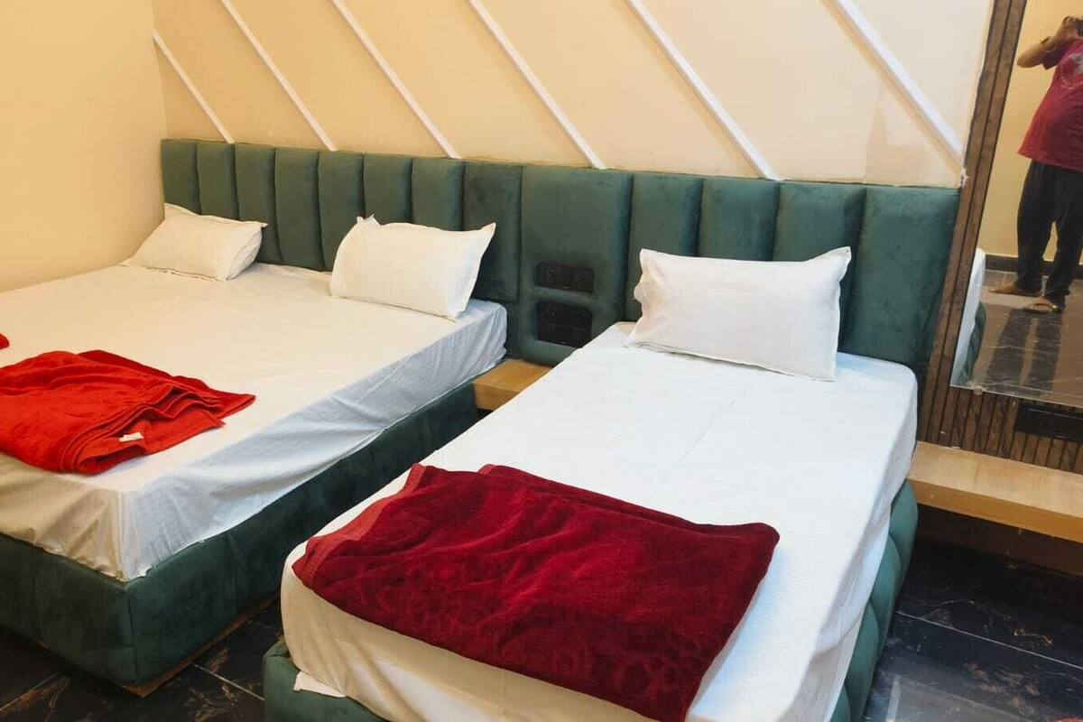 Dos camas individuales con cabeceros verdes y ropa de cama blanca, mantas rojas sobre cada cama, y un espejo que refleja parte de la habitación.