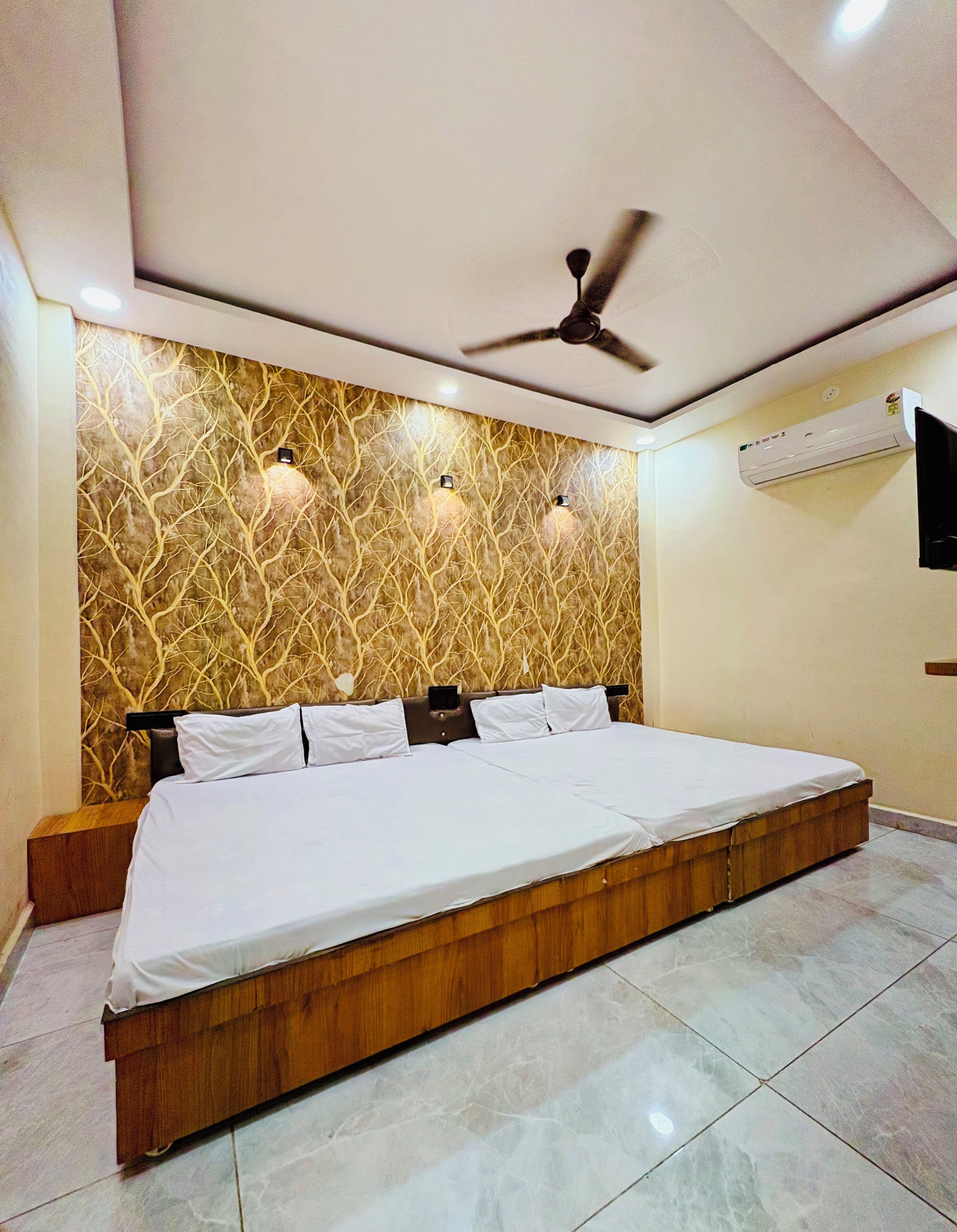 A bedroom with a large bed, a ceiling fan, wall-mounted lights, and an air conditioning unit.
