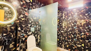 A modern bathroom with a geometric tile backsplash, a wooden ceiling, and a glass partition. - Hotel Naagshree (Ujjain)