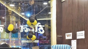 A reception desk with a striped chair, a wooden counter, and a glass window with balloons. - Hotel Naagshree (Ujjain)