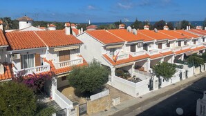 A row of white buildings with orange tiled roofs, balconies, and a clear view of the sea.