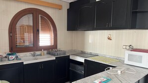 A kitchen with dark cabinets, a white countertop, a window with blinds, and a microwave.