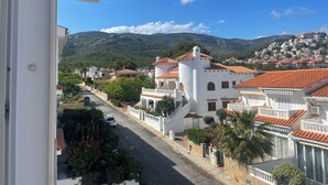 A residential street with white buildings, a prominent tower, and a mountainous backdrop.