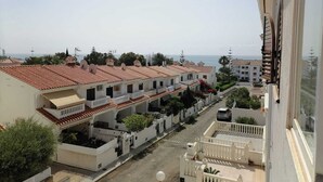 A residential area with terracotta-tiled buildings, balconies, and a view of the sea.