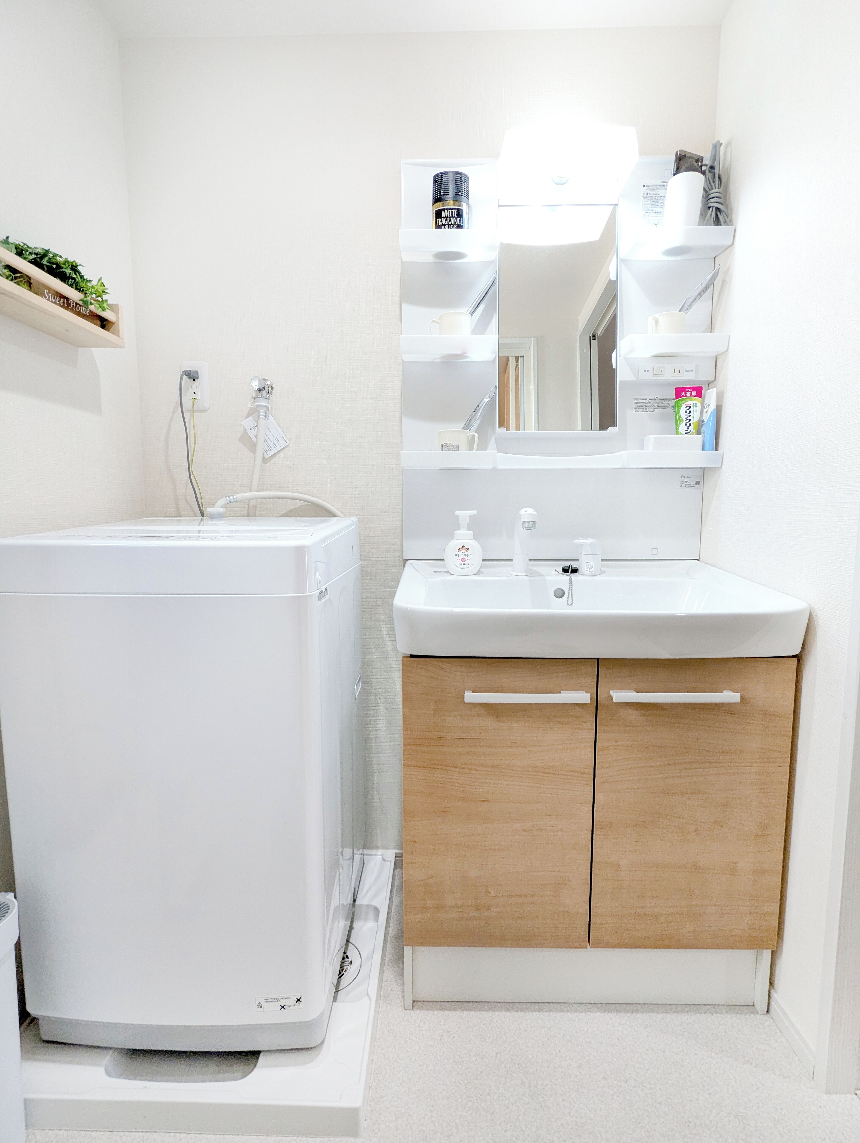 A bathroom with a white washing machine, a sink with a mirror above it, and wooden cabinets.