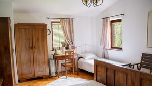 A bedroom with a wooden wardrobe, a desk with a chair, a bed with a white mattress, and a window with curtains.