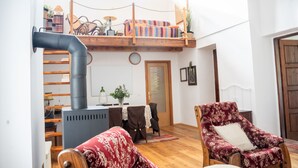 A loft-style room with a wooden ceiling, a built-in sofa, a red patterned armchair, and a small table with a chair.