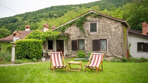 A rustic stone house with ivy, two striped chairs, and a small table in the front yard.