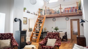A cozy living room with a wooden loft, a fireplace, and a dining area.