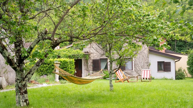 A grassy area with a hammock, two striped beach chairs, and a stone building with a thatched roof.