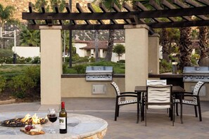 Un patio exterior con dos parrillas de barbacoa, un hogar con leña ardiendo y una mesa con sillas.