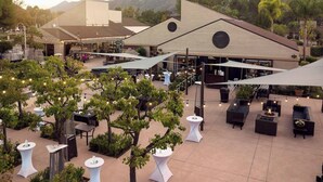 Un espace extérieur aménagé en terrasse, avec des tables et des chaises rondes, entouré d’arbres et bordé par un bâtiment doté d’un toit en pente.