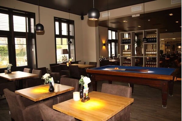 Relax in a spacious room with a pool table, seating areas, and a bar with a selection of drinks.