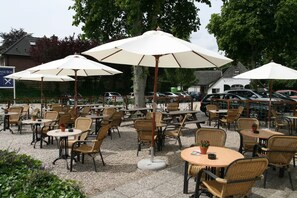 Relax in a shaded outdoor seating area with tables and wicker chairs.