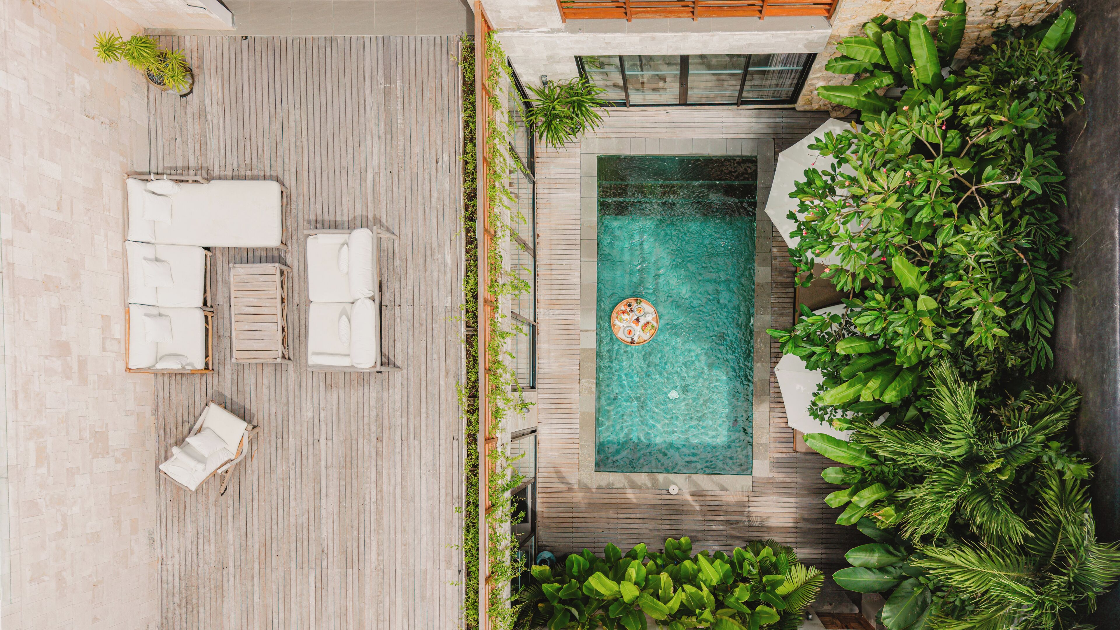 A rooftop pool with lounge chairs, surrounded by greenery and a wooden deck.