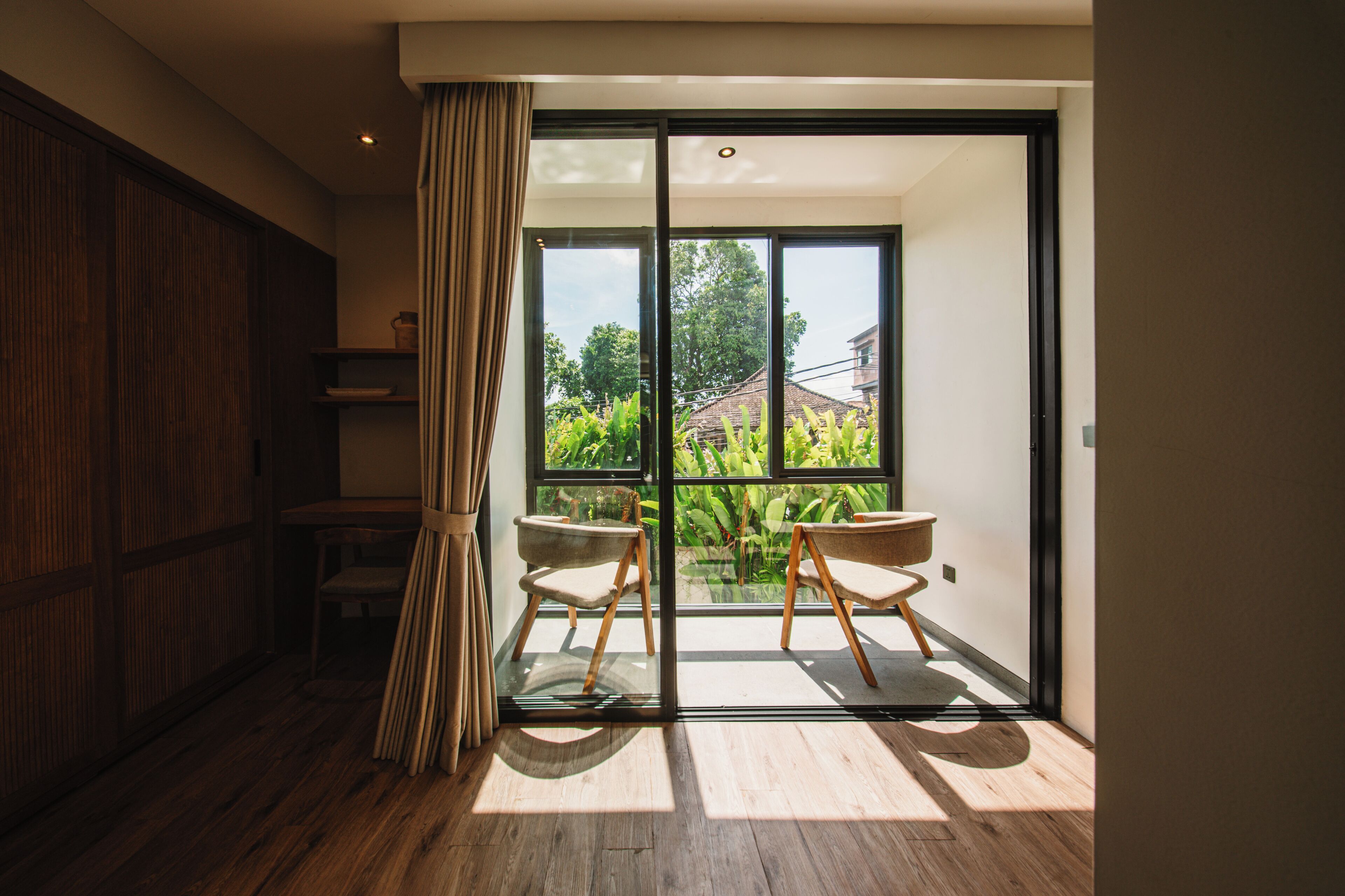 Een kamer met een schuifglazen deur die leidt naar een balkon, houten vloeren en twee stoelen.