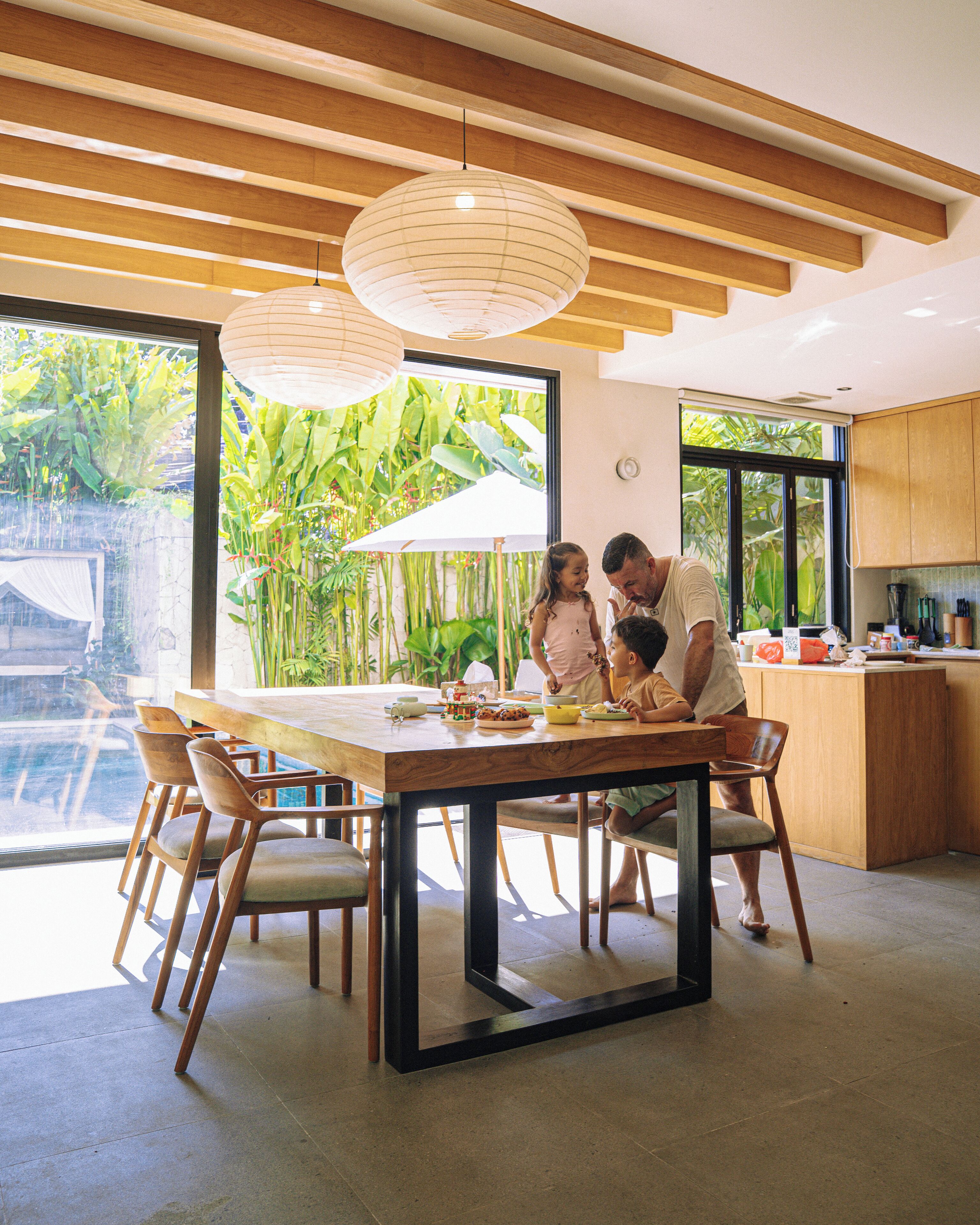 A modern kitchen with wooden cabinets, a dining table with chairs, and a view of a swimming pool.