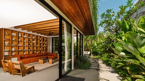 Une maison moderne dotée d’une grande porte vitrée qui donne sur un espace de vie comprenant un canapé et des étagères en bois.
