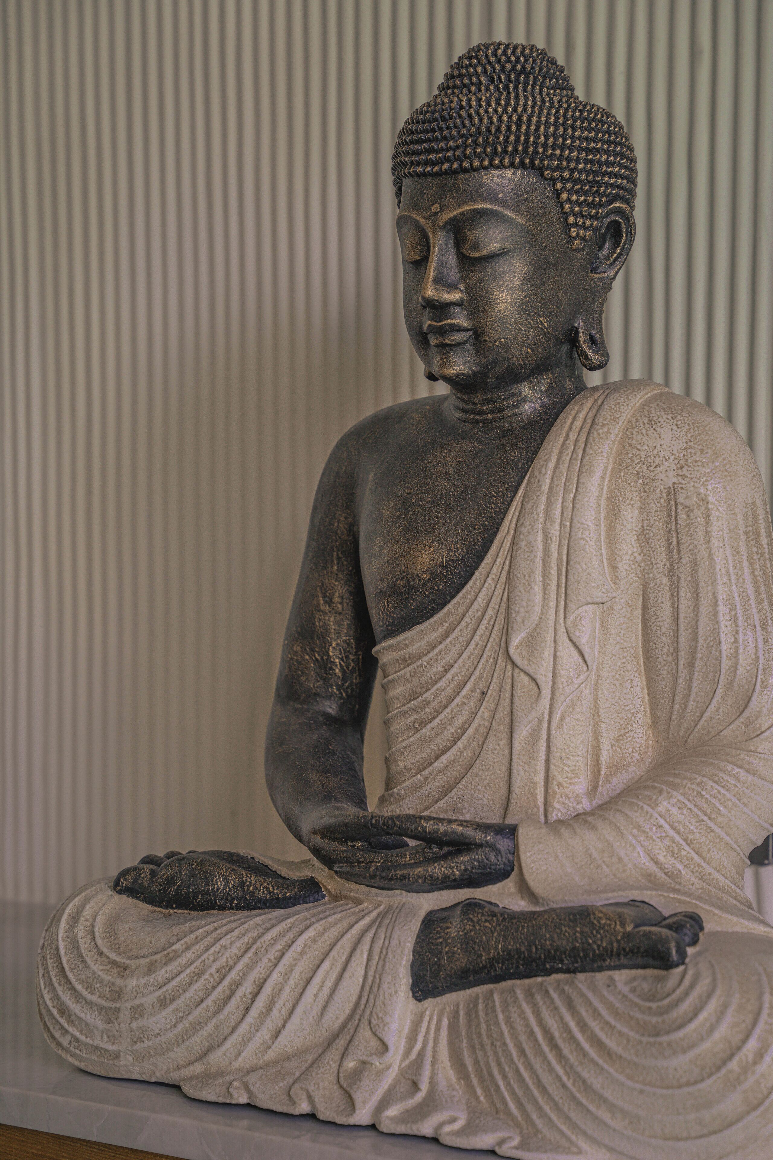 A statue of a seated figure with a draped robe, set against a vertical striped background.