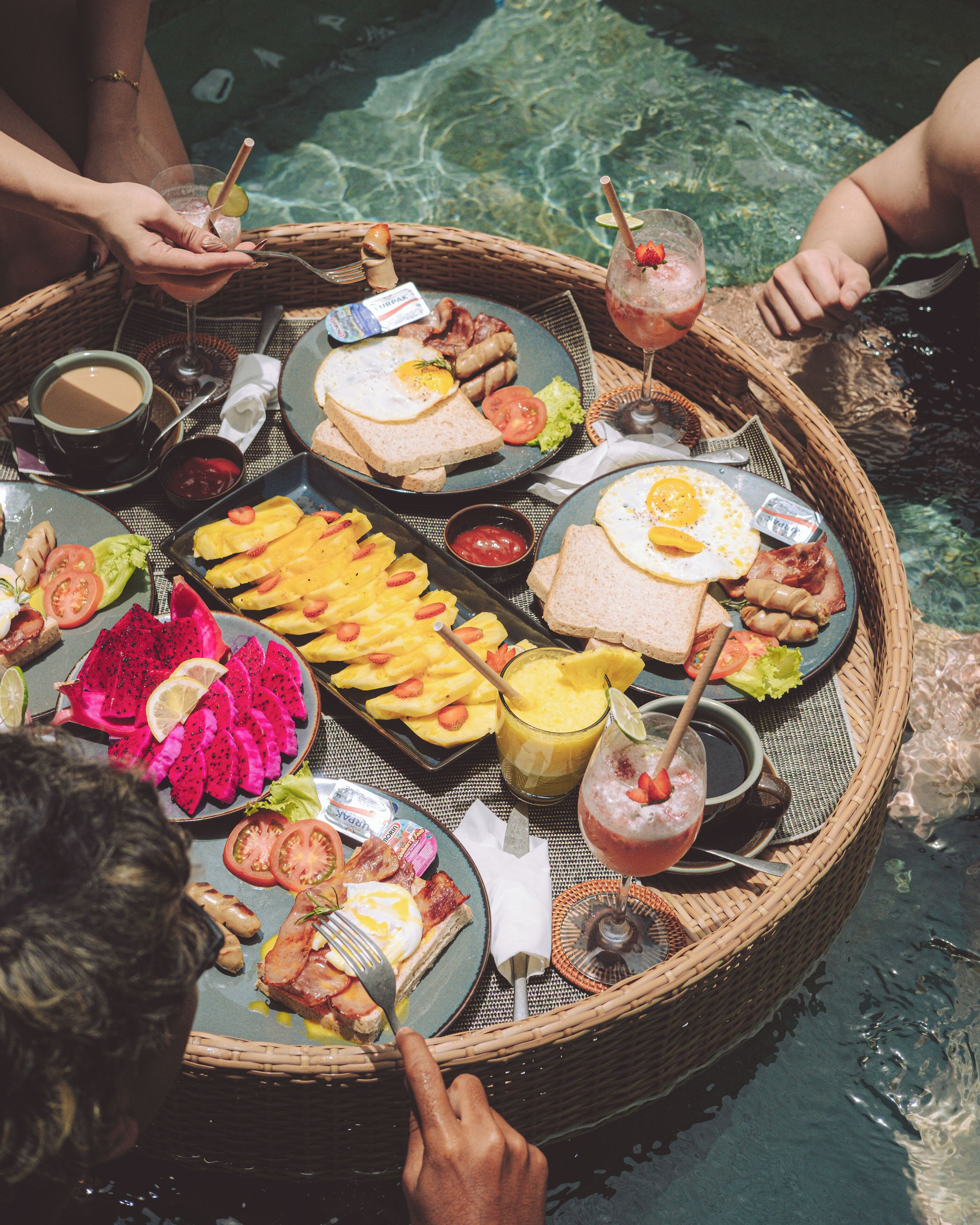 A round table with a variety of food items and drinks, surrounded by a pool.