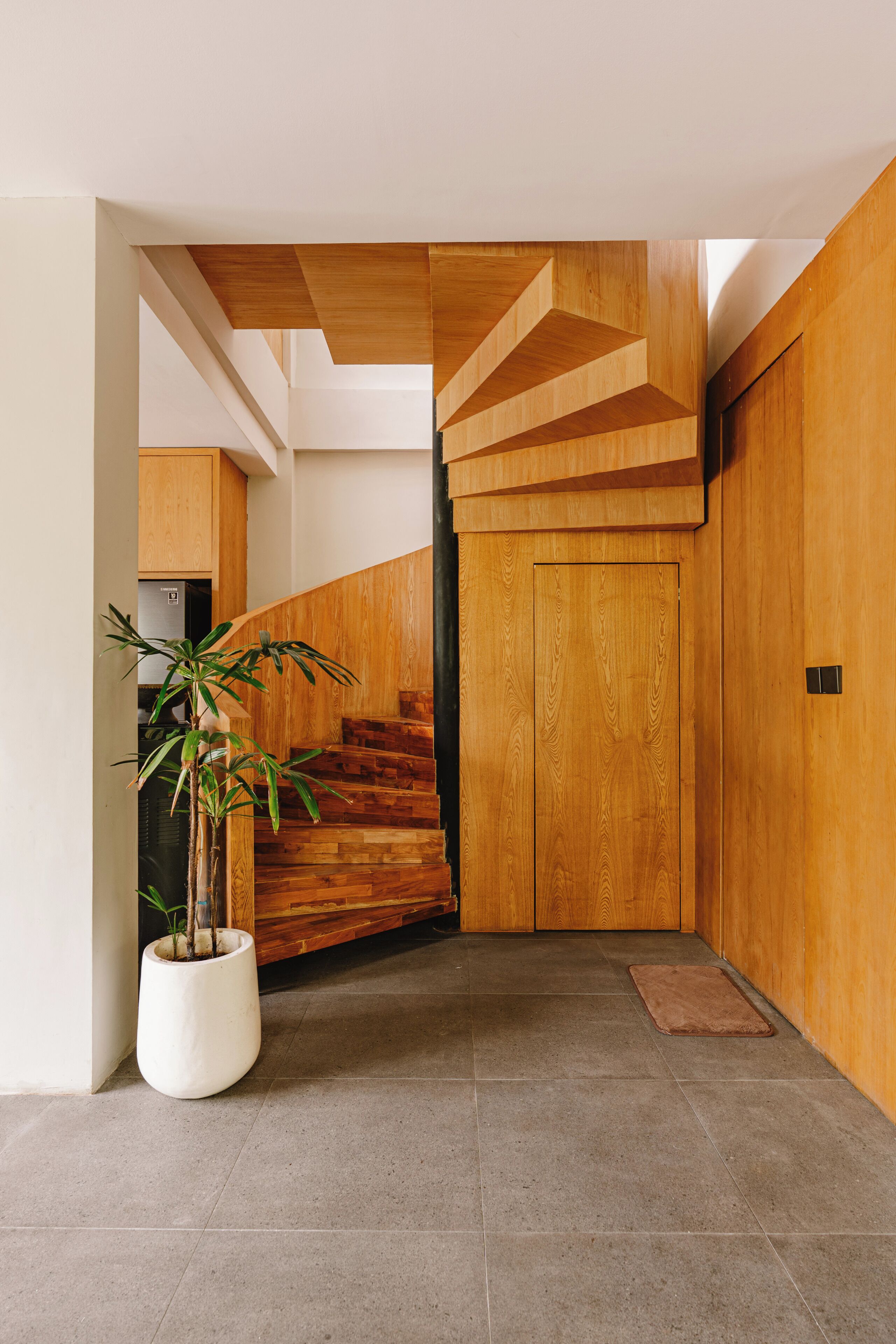 A modern interior with a wooden staircase, a potted plant, and a tiled floor.