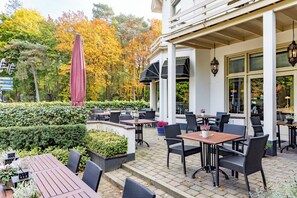 Enjoy dining or socializing in this outdoor patio area with tables and chairs, surrounded by lush greenery and beautifully lit by lantern-style lights.